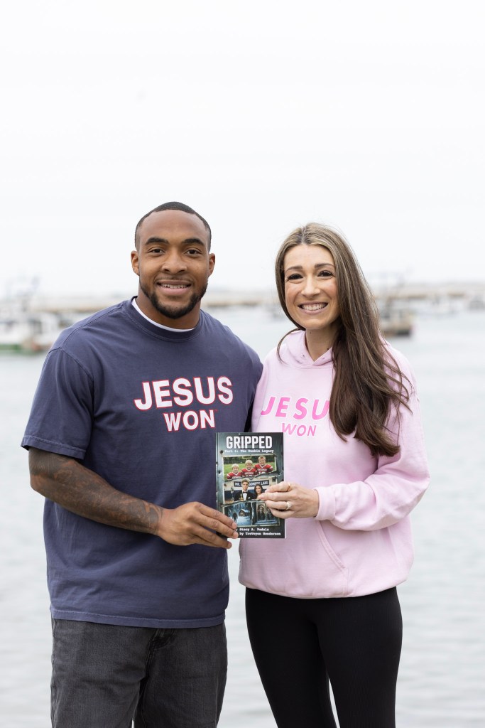 Two individuals posing by the waterfront, one man wearing a navy t-shirt that says 'JESUS WON' and one woman wearing a pink hoodie with the same text. They are holding a magazine titled 'GRIPPED'.